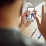 Close-up of a man waving to his doctor during video call over smart phone. Focus is on touchscreen.